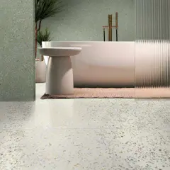 Baño moderno con bañera exenta y grifería dorada, sobre suelos de terrazo claros y paredes con el mismo acabado en tono verde.
