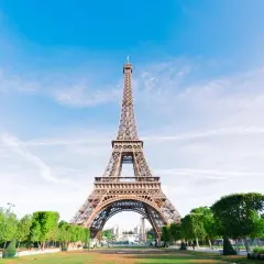 La icónica Torre Eiffel, un ejemplo del estilo arquitectónico de la época, se alza majestuosa bajo un cielo azul con nubes dispersas.