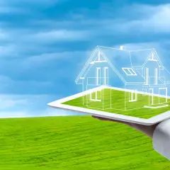 Diseño de una casa ecológica autosuficiente proyectada sobre una tablet, con un paisaje verde y cielo azul de fondo.