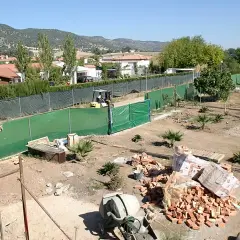 Terreno con materiales para construir dos casas. Se ven ladrillos, cementera y una excavadora.