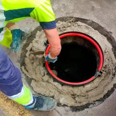 Trabajador instala un anillo rojo en una alcantarilla. Averigua cuanto cuesta conectarse al alcantarillado.