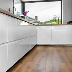 Cocina moderna con armarios blancos brillantes y encimeras de madera. El suelo vinílico SPC de madera aporta calidez y estilo.