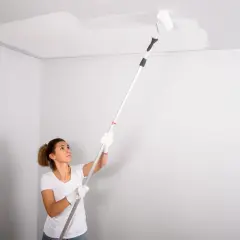Mujer pintando el techo con rodillo. La pregunta de si que se pinta primero el techo o las paredes es clave en esta tarea.