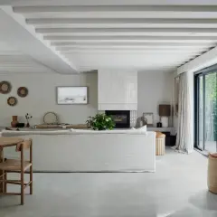 Salón moderno con suelo de porcelánico que es perfecto para crear un ambiente sereno. Sofá blanco, chimenea y grandes ventanales.