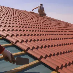 Trabajadores instalan tejas rojas en un tejado, mostrando las formas de tejados de casas.