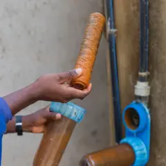 Persona con traje azul revisa un filtro de agua muy sucio, parte de la red de saneamiento de una vivienda unifamiliar.