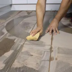 Man limpiando suelo porcelánico después de obra con una esponja, eliminando restos de cemento y polvo.