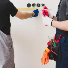 Dos electricistas trabajan en la instalación eléctrica de una vivienda, midiendo y anotando detalles.