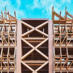 Estructura de madera con celosías y plantas, mostrando elementos de arquitectura moderna contra un cielo azul.