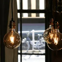 Lámparas Edison con filamentos visibles, creando una atmósfera cálida. La luz tenue sugiere pocos lúmenes por m2, ideal para un ambiente acogedor.