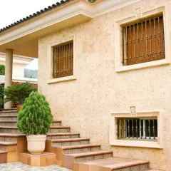 Fachada de casa con escaleras y plantas. Los distintos tipos de pared de piedra y detalles ornamentales resaltan la arquitectura.
