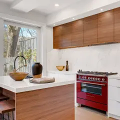 Cocina moderna con isla central, encimeras de cuarzo, gabinetes de madera y estufa roja. Un ejemplo de diseño de espacios interiores funcional y elegante.