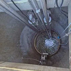 Vista superior de una estación de bombeo con tuberías y cadenas. El agua turbulenta llena el pozo, parte de la red de evacuación de aguas residuales y pluviales.