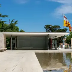 Pabellón de Mies van der Rohe, con su diseño minimalista, reflejos en el agua y una bandera catalana ondeando.