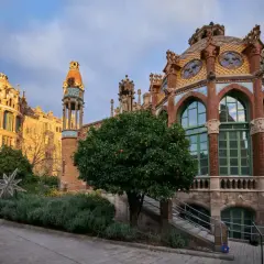 Edificios modernistas con cúpulas coloridas y arcos, rodeados de vegetación y un árbol frutal.