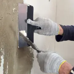Manos enguantadas aplican yeso para sanear pared con llana.