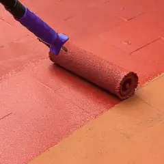 Rodillo morado pintando un suelo de baldosas con pintura roja, renovando el espacio.