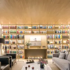 Un salón moderno con una gran librería iluminada, chimenea y sofás. Un diseñador de espacios ha creado un ambiente acogedor y elegante.