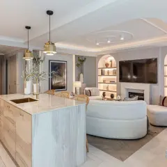 Cocina y sala de estar modernas con isla de cocina de madera, sofá curvo y estanterías iluminadas. La luz artificial crea un ambiente acogedor.