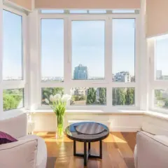 Sofá blanco con cojín morado, mesa negra y jarro de tulipanes blancos, disfrutando de los distintos tipos de luz natural que entran por los grandes ventanales.