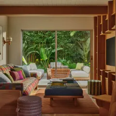 Sofá colorido y otomanas en una sala de estar con un sistema de iluminación cálido que ilumina el arte de pared y la vista al jardín.