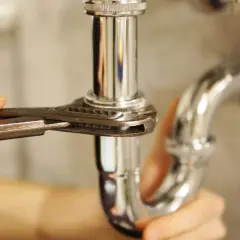 Mano ajustando tubería cromada con llave inglesa, parte de un arqueta sifónica esquema.