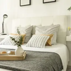Cabecero blanco tapizado, listo para inspirarte en cómo tapizar un cabecero. Cama con cojines a rayas y mostaza, bandeja con desayuno.