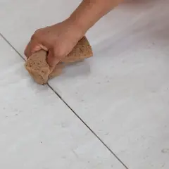 Mano aplicando lechada a las juntas de baldosas. Elige entre diversos colores de lechada para juntas para un acabado perfecto.