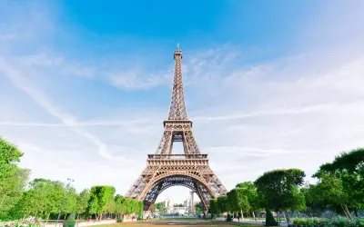 La icónica Torre Eiffel, un ejemplo del estilo arquitectónico de la época, se alza majestuosa bajo un cielo azul con nubes dispersas.