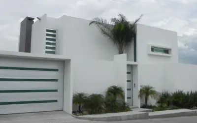 Casa moderna con líneas limpias y un estilo arquitectónico minimalista. Puerta de garaje blanca con detalles verdes.