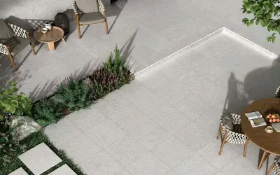 Terraza moderna con mobiliario de exterior y vegetación. El suelo está cubierto por un elegante **azulejo rectificado** de tonos grises, creando un espacio acogedor.