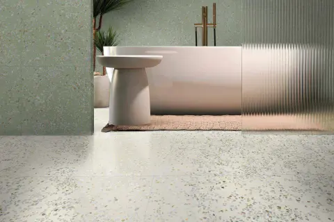 Baño moderno con bañera exenta y grifería dorada, sobre suelos de terrazo claros y paredes con el mismo acabado en tono verde.