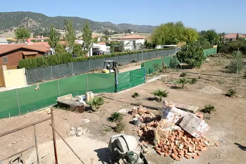 Terreno con materiales para construir dos casas. Se ven ladrillos, cementera y una excavadora.