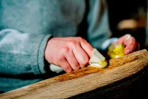 Manos aplicando cera a un trozo de madera. El proceso de **decapar madera** revela su belleza natural.