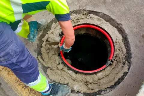 Trabajador instala un anillo rojo en una alcantarilla. Averigua cuanto cuesta conectarse al alcantarillado.