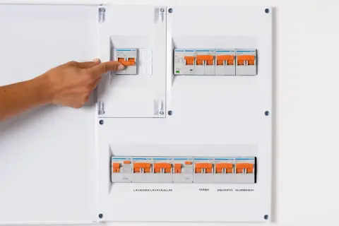 Panel de circuitos vivienda con interruptores naranjas. Una mano activa uno de los interruptores.