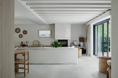 Salón moderno con suelo de porcelánico que es perfecto para crear un ambiente sereno. Sofá blanco, chimenea y grandes ventanales.