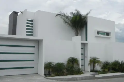 Casa moderna con líneas limpias y un estilo arquitectónico minimalista. Puerta de garaje blanca con detalles verdes.
