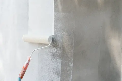 Rodillo aplicando imprimación pintura pared. La pared gris se transforma en blanco.