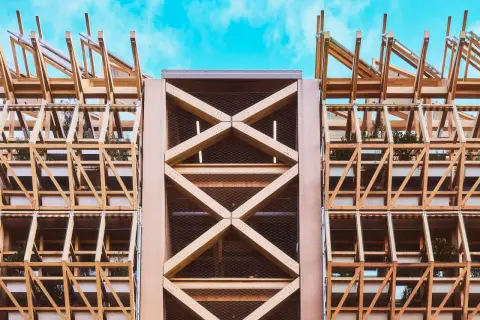 Estructura de madera con celosías y plantas, mostrando elementos de arquitectura moderna contra un cielo azul.