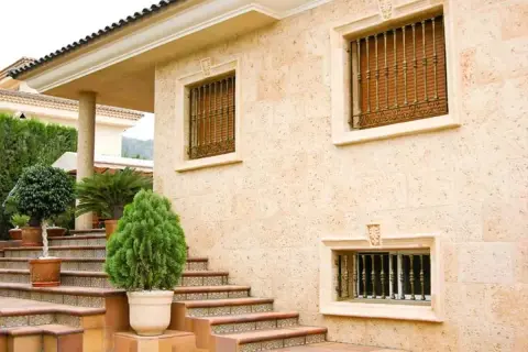 Fachada de casa con escaleras y plantas. Los distintos tipos de pared de piedra y detalles ornamentales resaltan la arquitectura.