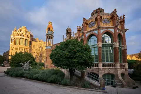Edificios modernistas con cúpulas coloridas y arcos, rodeados de vegetación y un árbol frutal.
