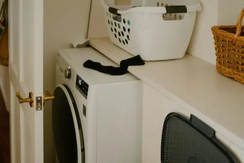 Lavadora blanca lista para instalar. Cesta de ropa y cesto de mimbre en la repisa superior.