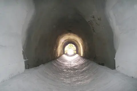 Interior de un túnel de drenaje, con luz al final. Podría ser un imbornal o un sumidero, ambos para evacuar agua.