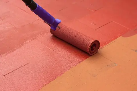 Rodillo morado pintando un suelo de baldosas con pintura roja, renovando el espacio.