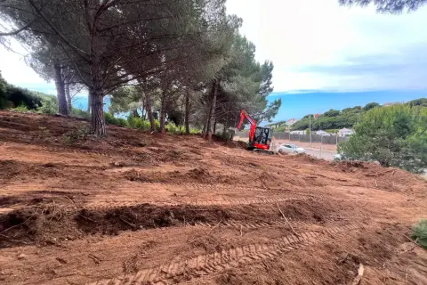 Excavadora roja trabaja en un solar urbano despejado, listo para construir.