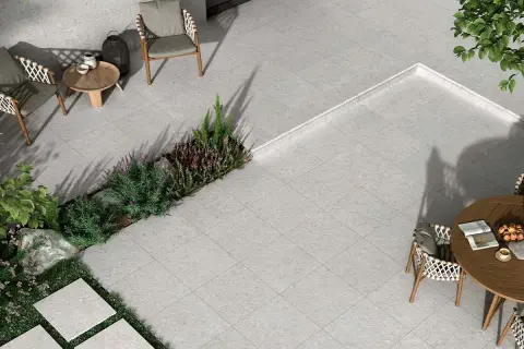 Terraza moderna con mobiliario de exterior y vegetación. El suelo está cubierto por un elegante **azulejo rectificado** de tonos grises, creando un espacio acogedor.