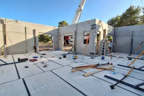Construcción de casa con paneles prefabricados. Se ve el suelo de hormigón, paredes levantadas y herramientas. ¿Cuánto cuesta terminar una casa en obra?