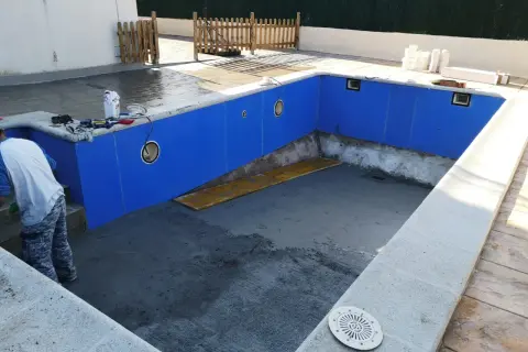 Piscina en construcción, paredes azules listas para recibir el gresite. Herramientas y materiales a un lado.