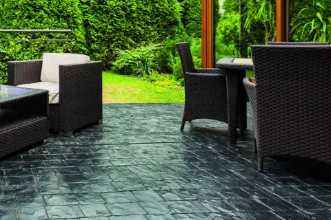 Terrazas con suelo de piedra oscura, muebles de mimbre y vegetación exuberante.